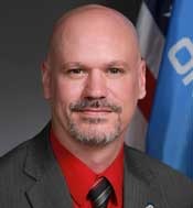 Chaplains in schools: Headshot man bald with graying brown mustache and beard in brown suit with red shirt and dark patterned tie